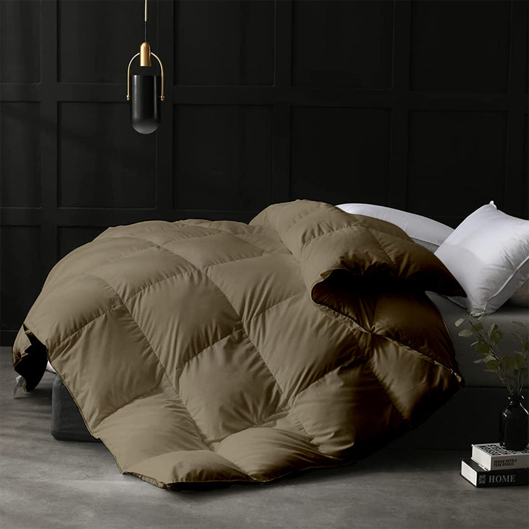 Beige quilt draped over a bed in a darkly decorated room with a lamp and books.