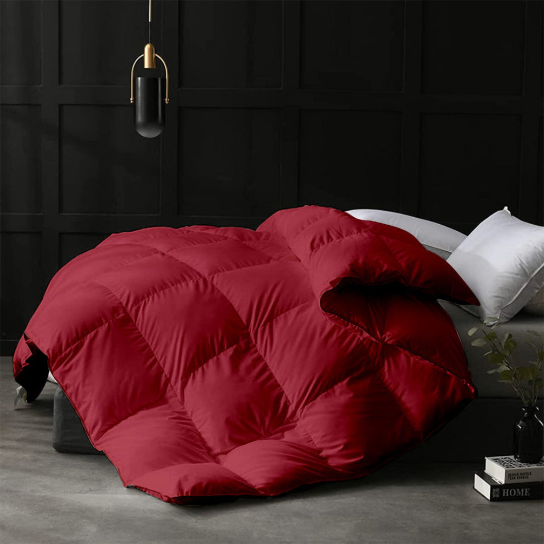 Red quilted comforter on a bed in a darkly decorated room.